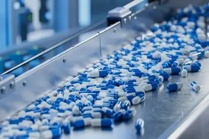 Blue and white capsules on a stainless steel conveyor belt in a pharmaceutical production line.